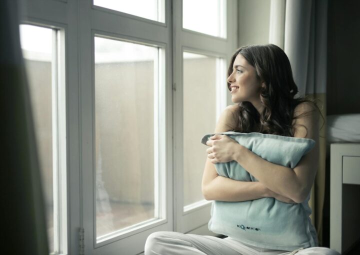 black haired woman hugging gray pillow near glass panel window