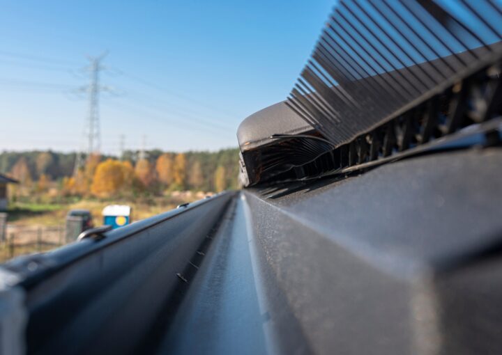 A metal, black gutter on a roof covered with ceramic tiles. Close up shot.