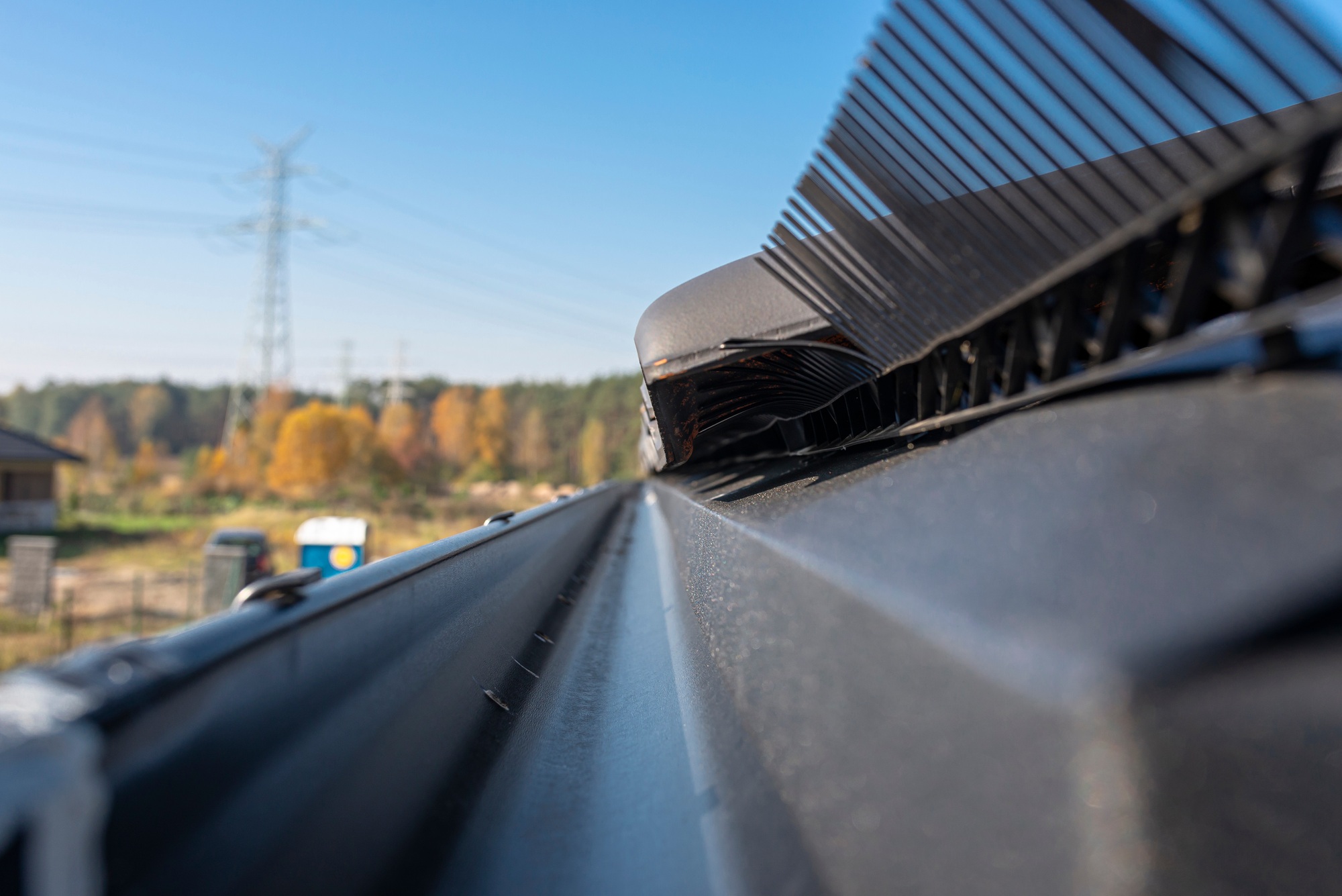 A metal, black gutter on a roof covered with ceramic tiles. Close up shot.